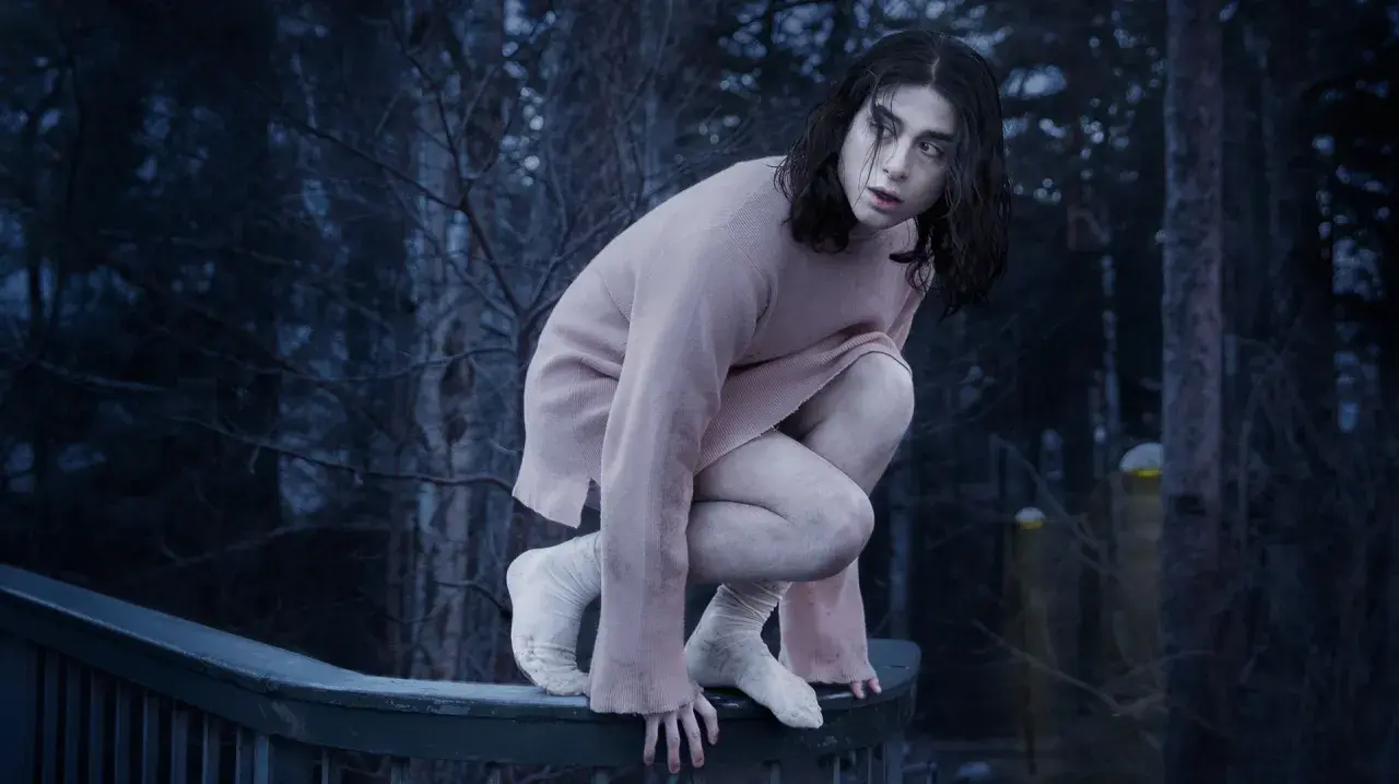 En svensk vampyr, Eli, hukar sig på ett räcke i en mörk skog.