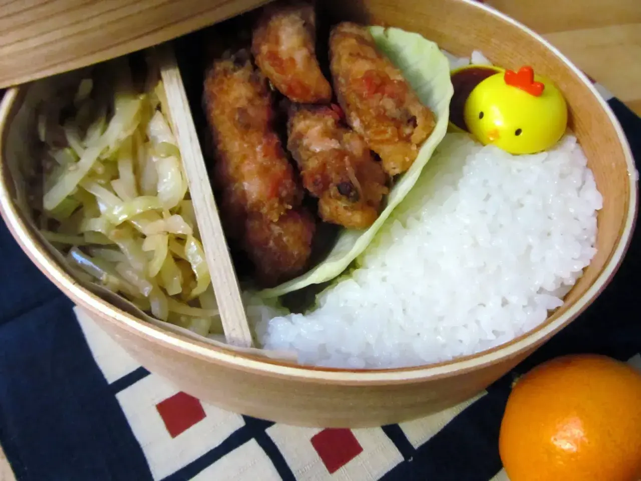 A delicious karaage bento box with crispy fried chicken, fluffy rice, pickled cabbage, and a cute chick-shaped decoration.
