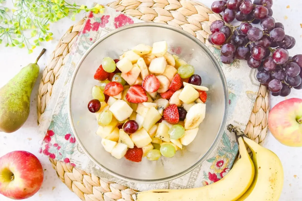 Un tazón lleno de colorida ensalada de frutas con fresas, uvas, plátano y trozos de manzana.