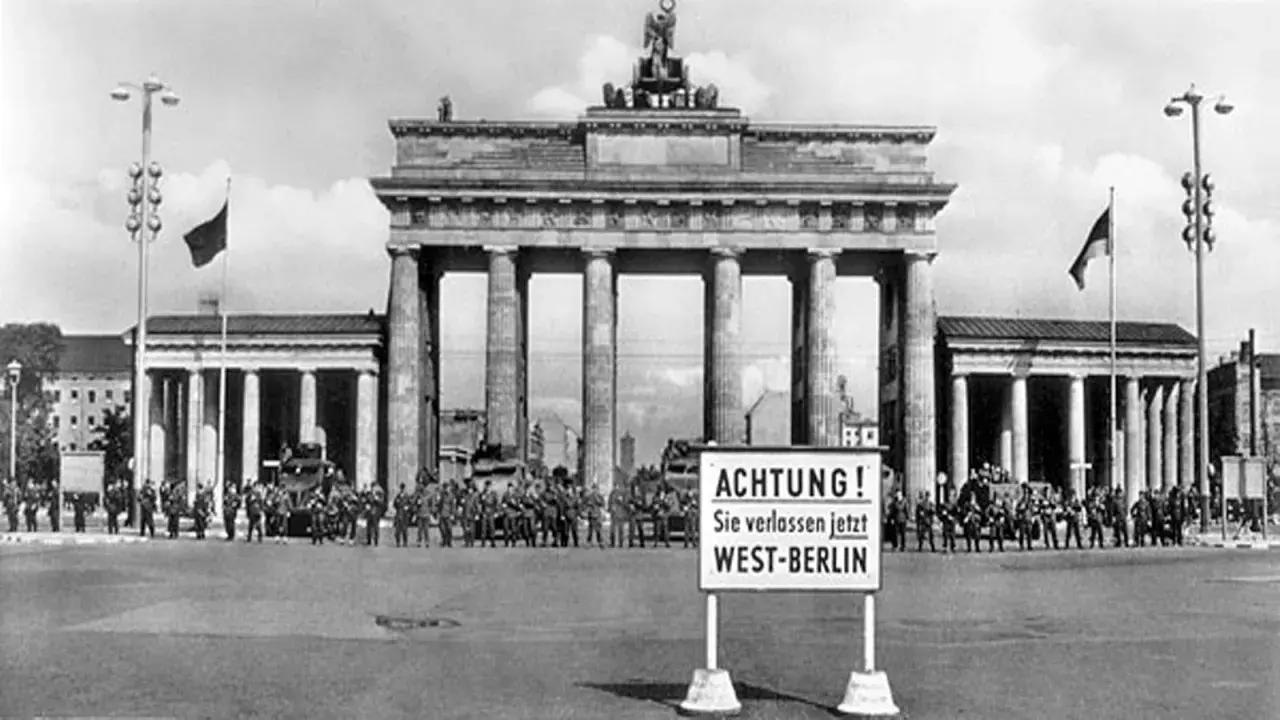 Brandenburger Tor, Soldaten und Panzer stehen Spalier. Ein Schild warnt: "ACHTUNG! Sie verlassen jetzt WEST-BERLIN". Ein Symbol des kalten Krieges.