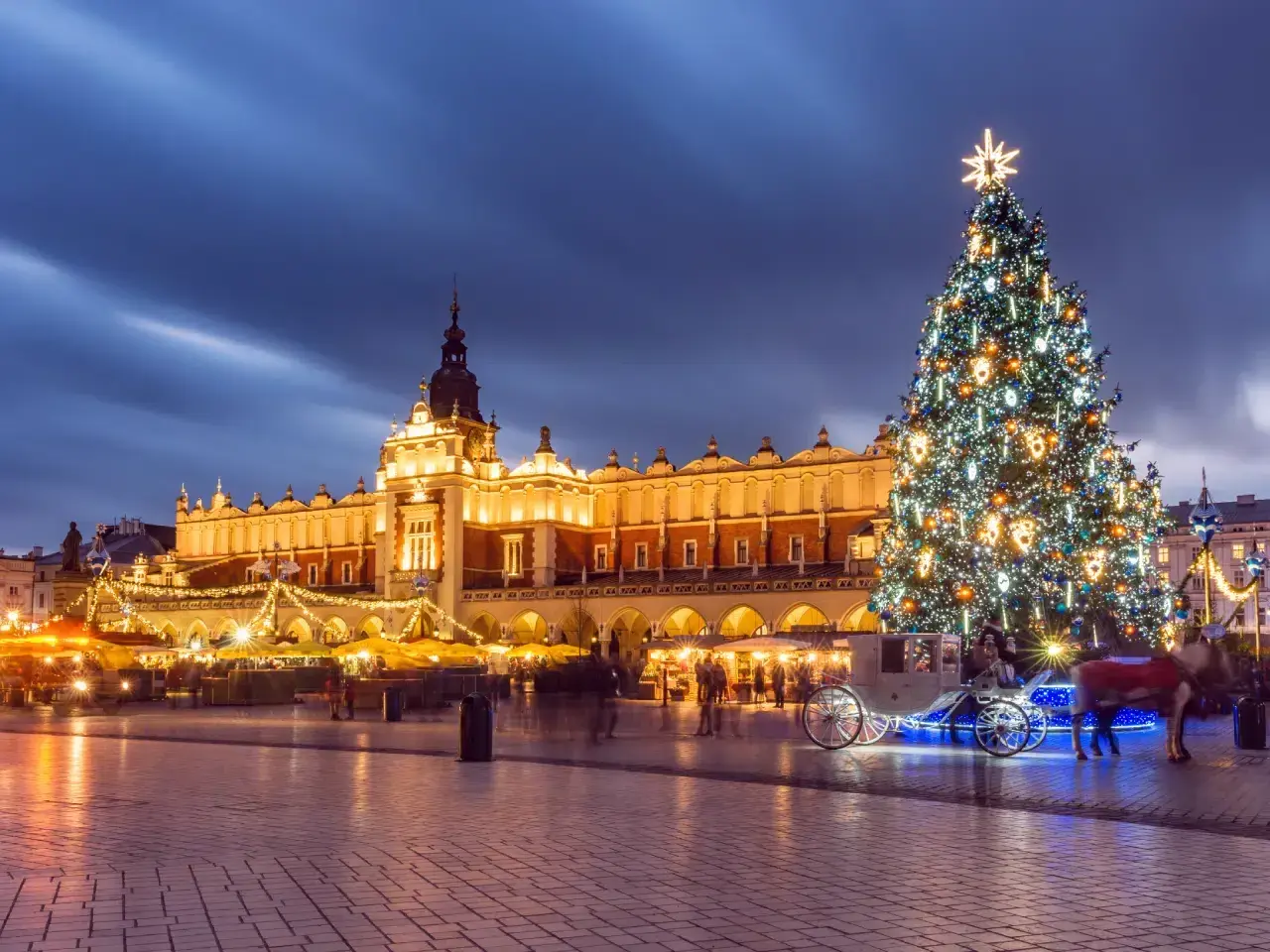 Magiczny jarmark bożonarodzeniowy krakow. Rozświetlona choinka, Sukiennice i karoca z końmi tworzą świąteczną atmosferę.