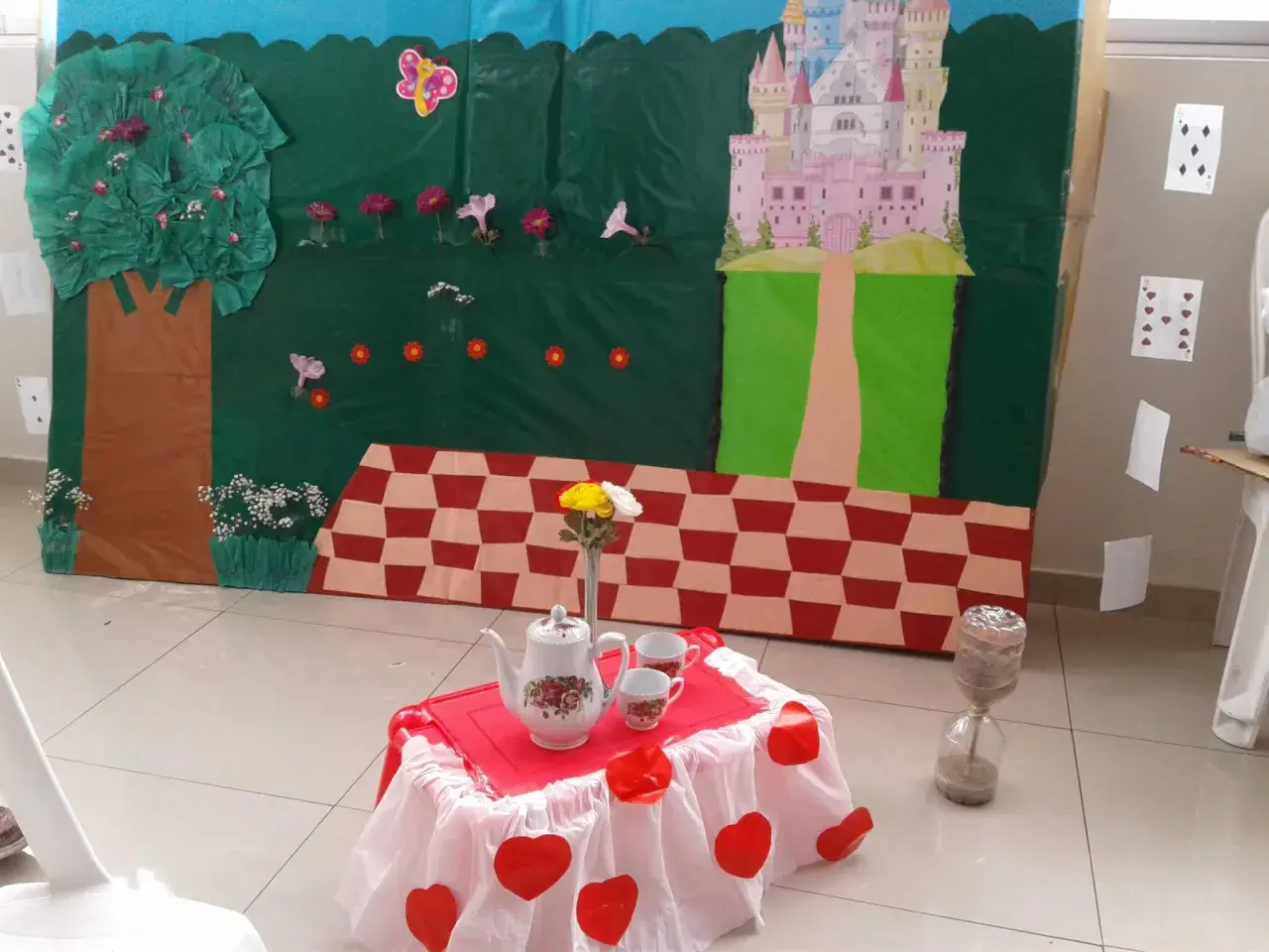 Escenario de manualidades alicia en el país de las maravillas con castillo, árbol, mesa de té y reloj de arena.