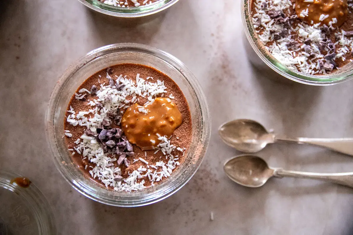 Chokladmousse med kokosflingor och kakaonibs, en härlig vegansk frukost. Två skedar ligger bredvid.