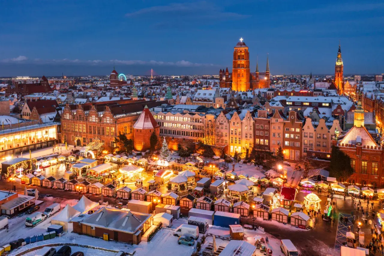 Gdańsk jarmark świąteczny nocą, z oświetlonymi kramami, karuzelą i zabytkową zabudową w tle.