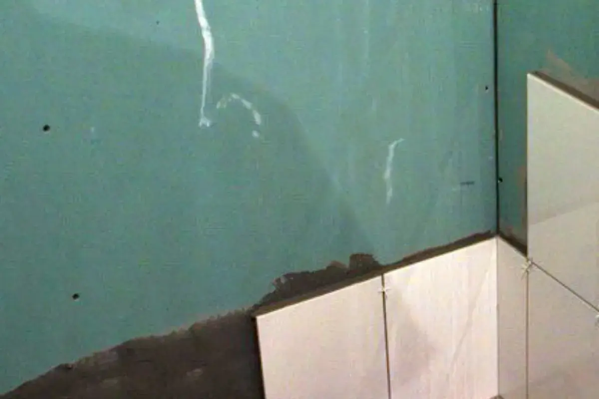 Angolo di una stanza con piastrelle su cartongesso in fase di posa. La parete verde è pronta per essere rivestita.