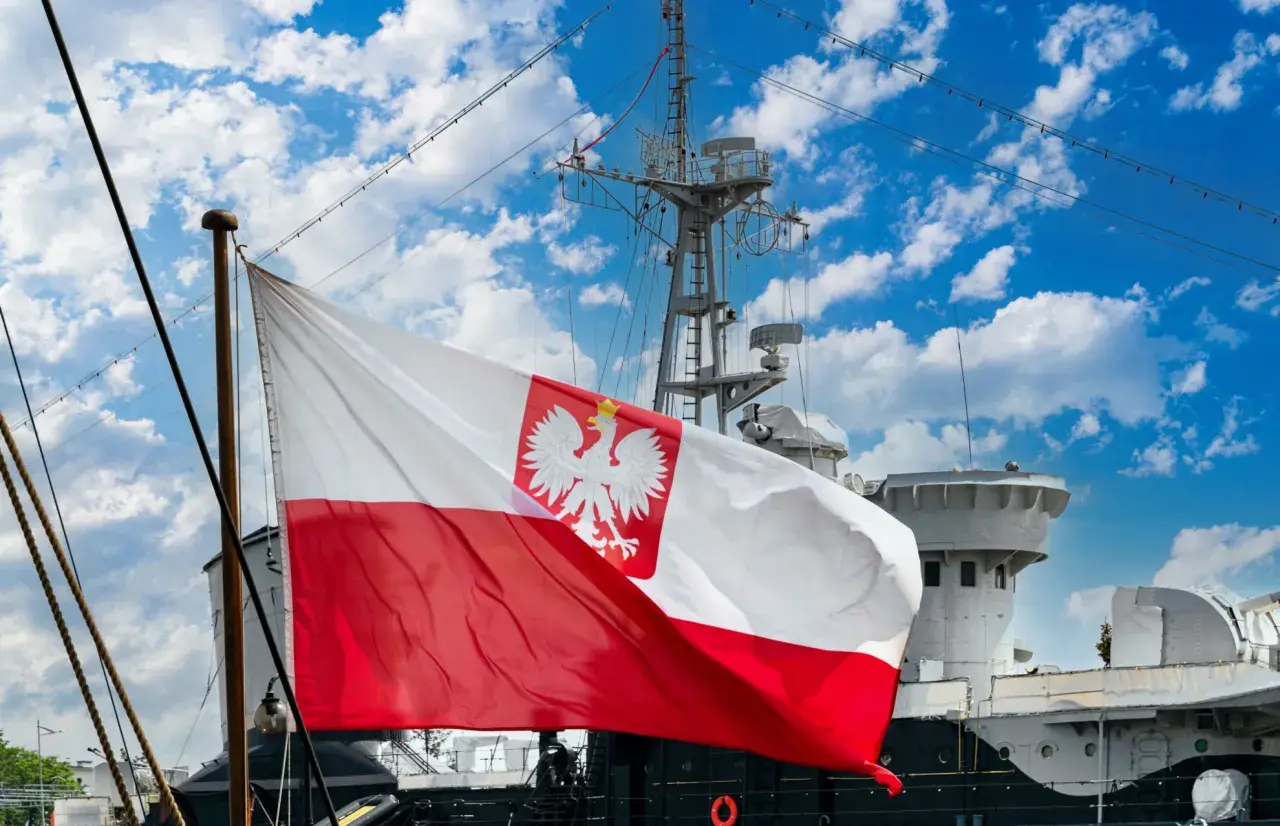 Flaga bandery z orłem dumnie powiewa na tle błękitnego nieba z chmurami, nad pokładem statku.
