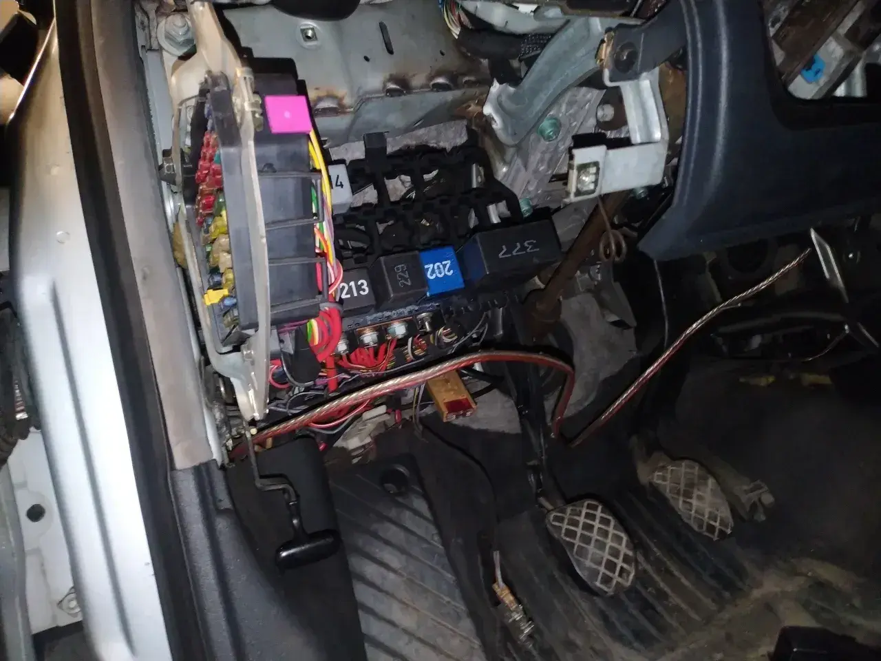 Widok na skrzynkę z bezpiecznikami i przekaźnikami w Audi A4 B6. Widać kolorowe bezpieczniki i wiązki przewodów.