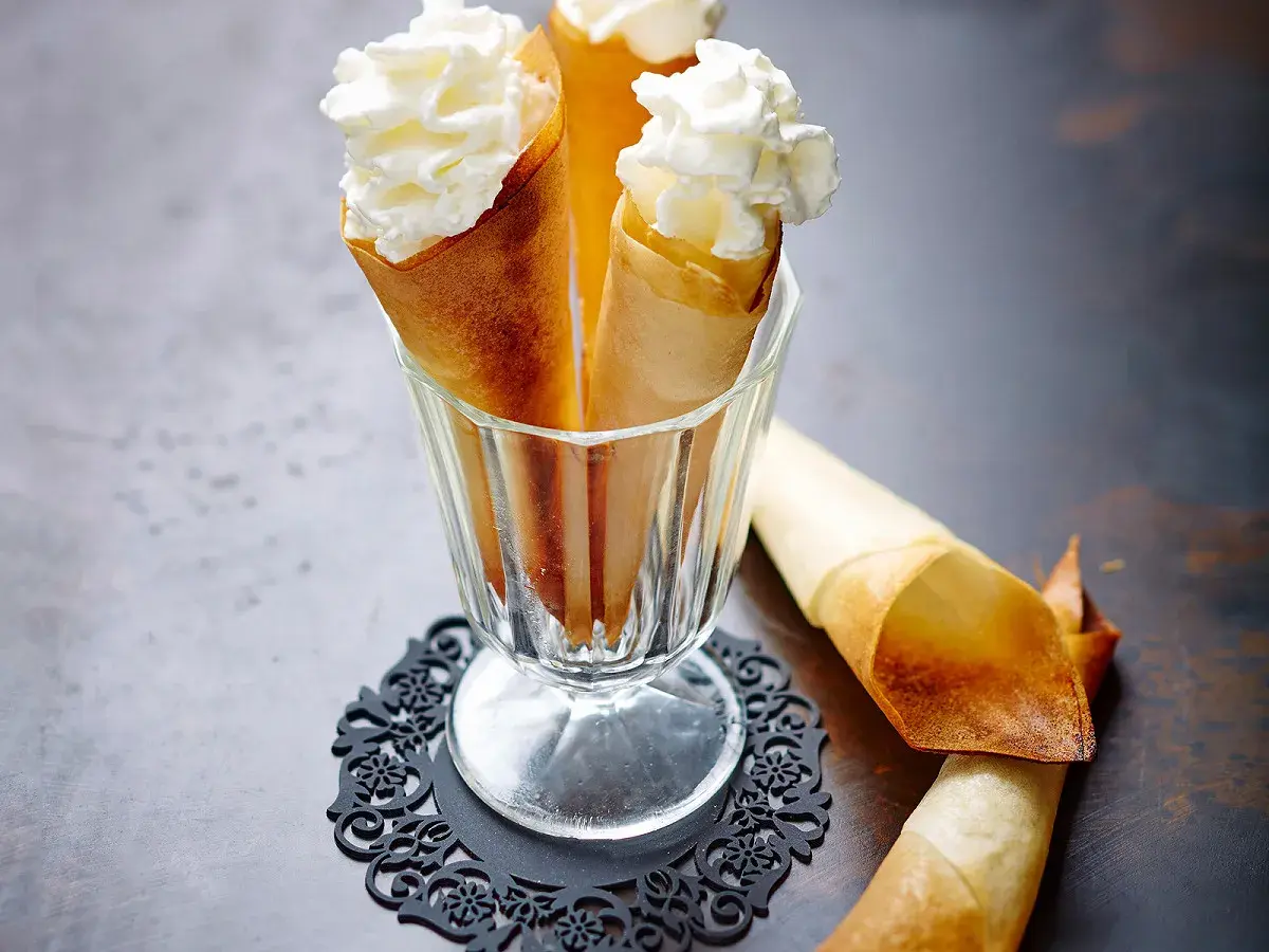 Délicieux cornets croustillants garnis de crème chantilly aérienne, prêts à être dégustés.