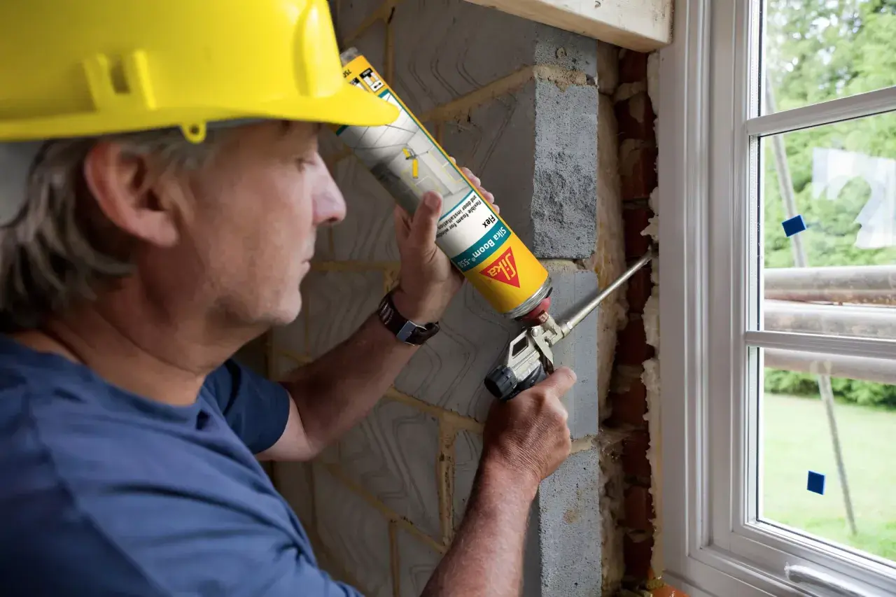 Obrero con casco amarillo aplica espuma expansiva para sellar ventanas exterior.