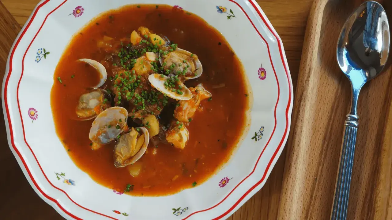 En skål med bouillabaisse med musslor och räkor, perfekt att servera med ett glas vin.