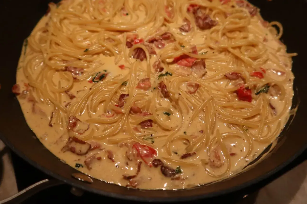 Krämig baconpasta i en stekpanna, med spaghetti och bitar av knaperstekt bacon.