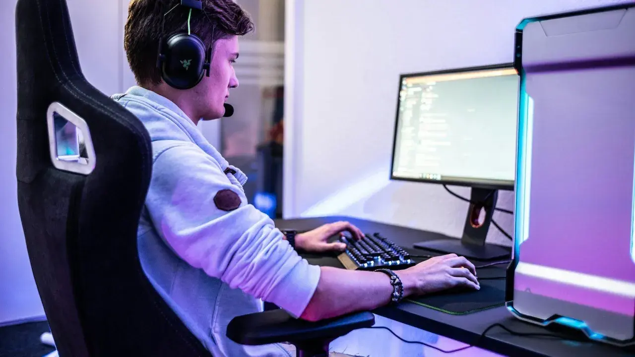 Ein junger Mann mit Headset spielt am PC. Er fragt sich vielleicht, was bedeutet gg im Chat.