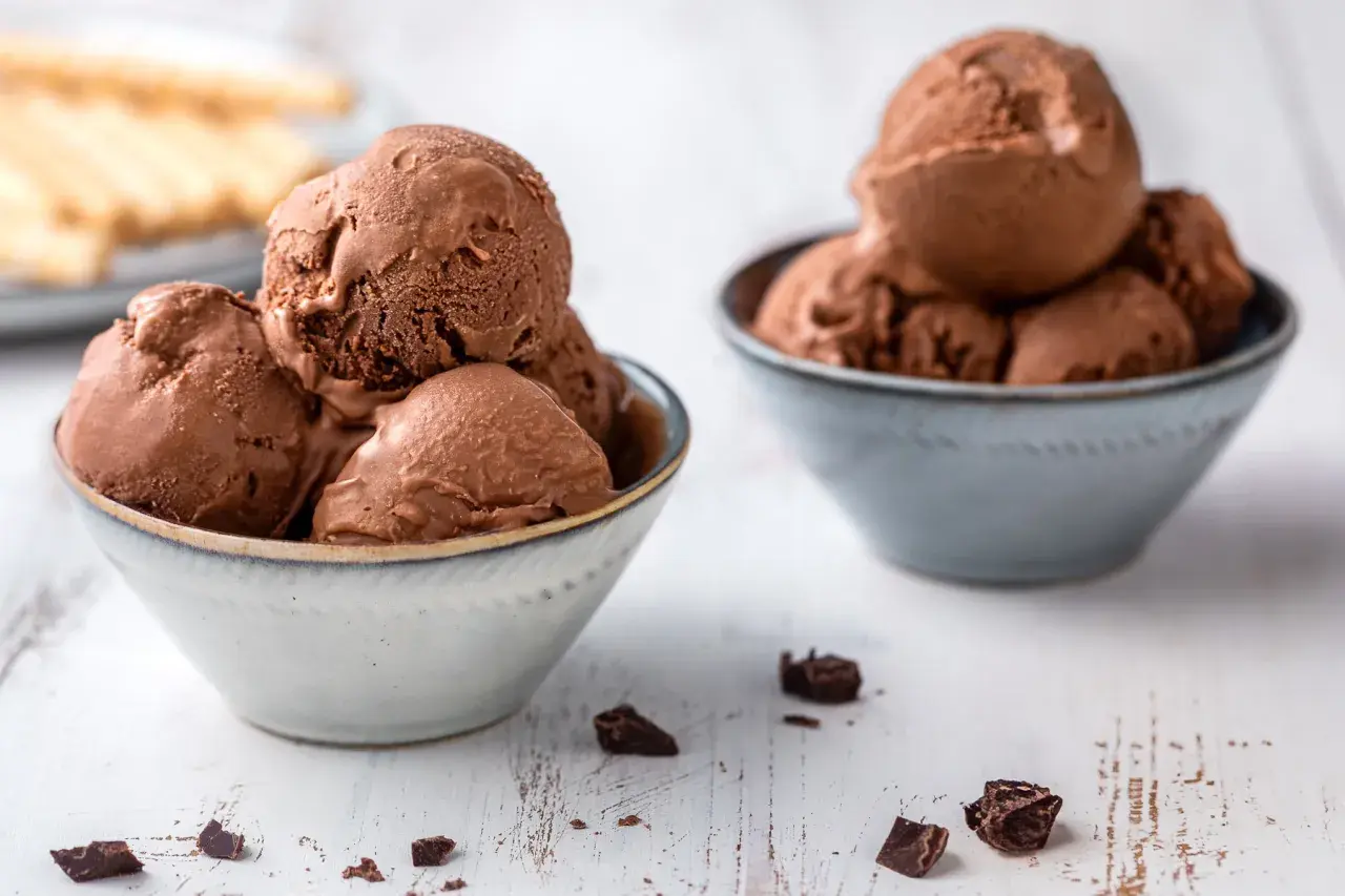Due ciotole piene di cremoso gelato al cioccolato, con pezzi di cioccolato sparsi sul tavolo.