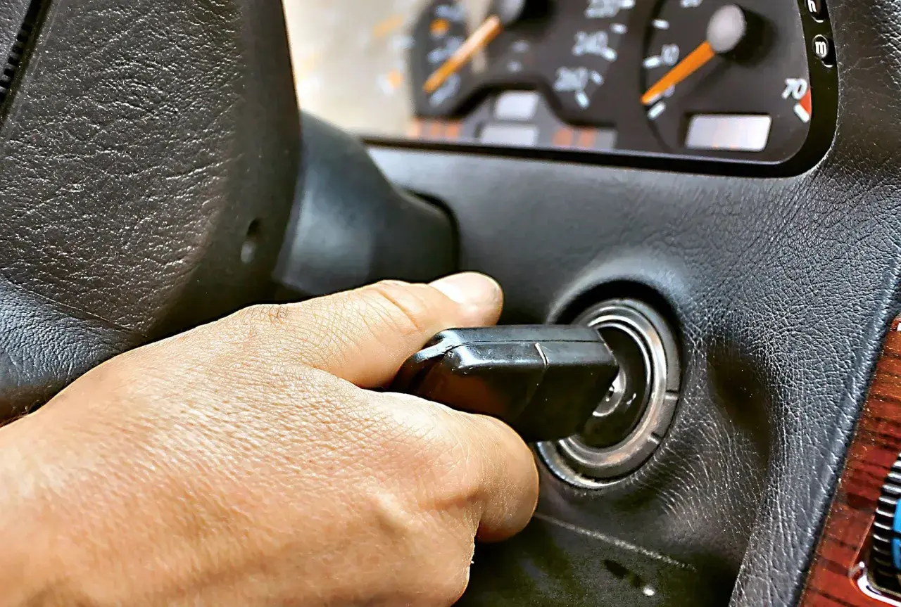 Dłoń przekręca kluczyk w stacyjce. Auto odpala i gaśnie, co sugeruje problem z zapłonem lub paliwem.