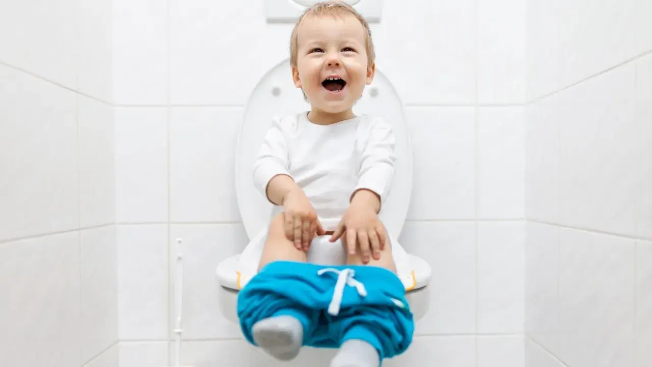 Bambino felice sul water, pantaloni abbassati, pronto per la sua prima cacca nel water.