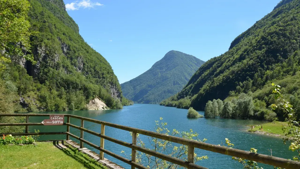 Il lago del Mis, incastonato tra montagne verdi e rigogliose, offre uno spettacolo mozzafiato con le sue acque azzurre e il cielo limpido.