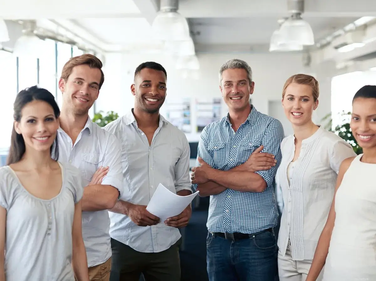 A diverse team smiles confidently, showcasing what employee engagement looks like. They stand together in a bright office, radiating positivity and collaboration.