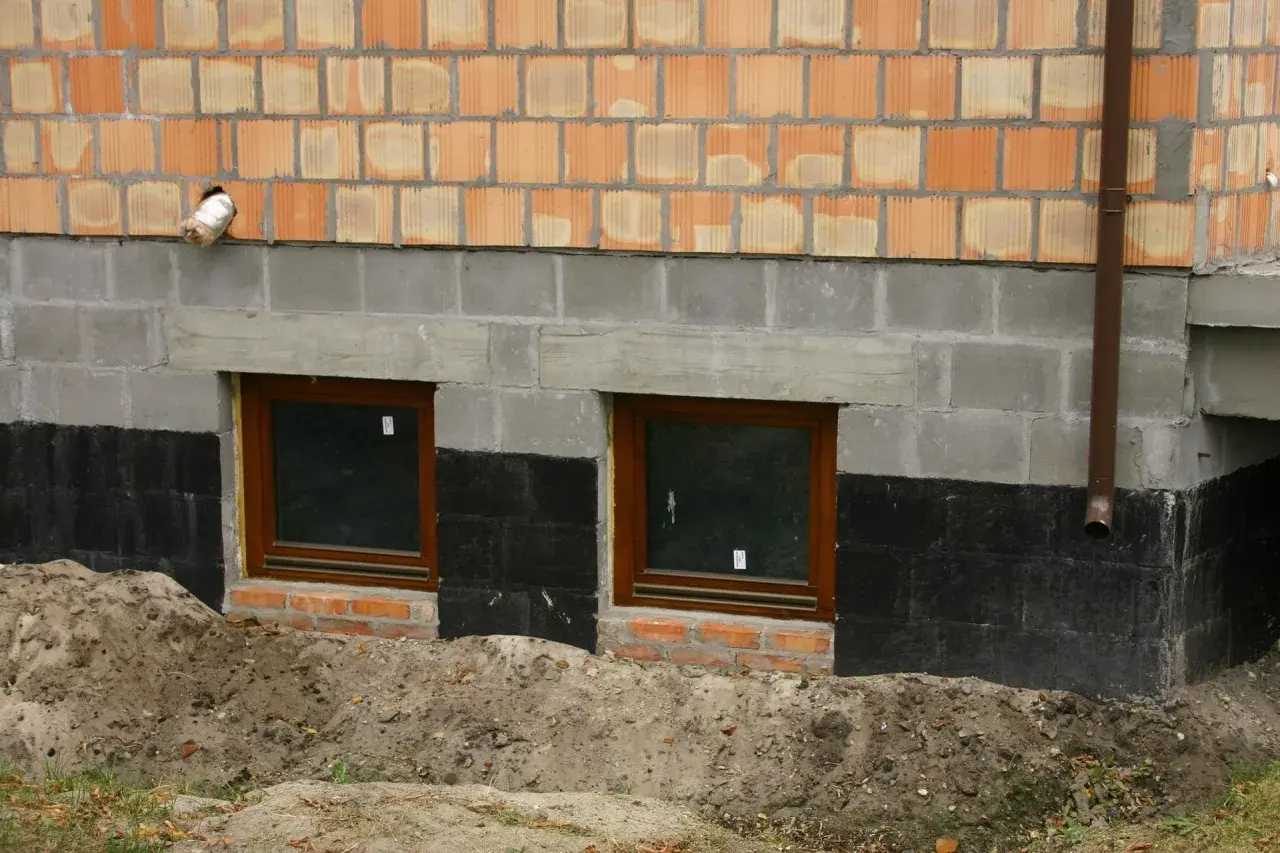 Wzmocnienie fundamentów w starym domu: nowe okna piwniczne, izolacja i warstwa cegieł.