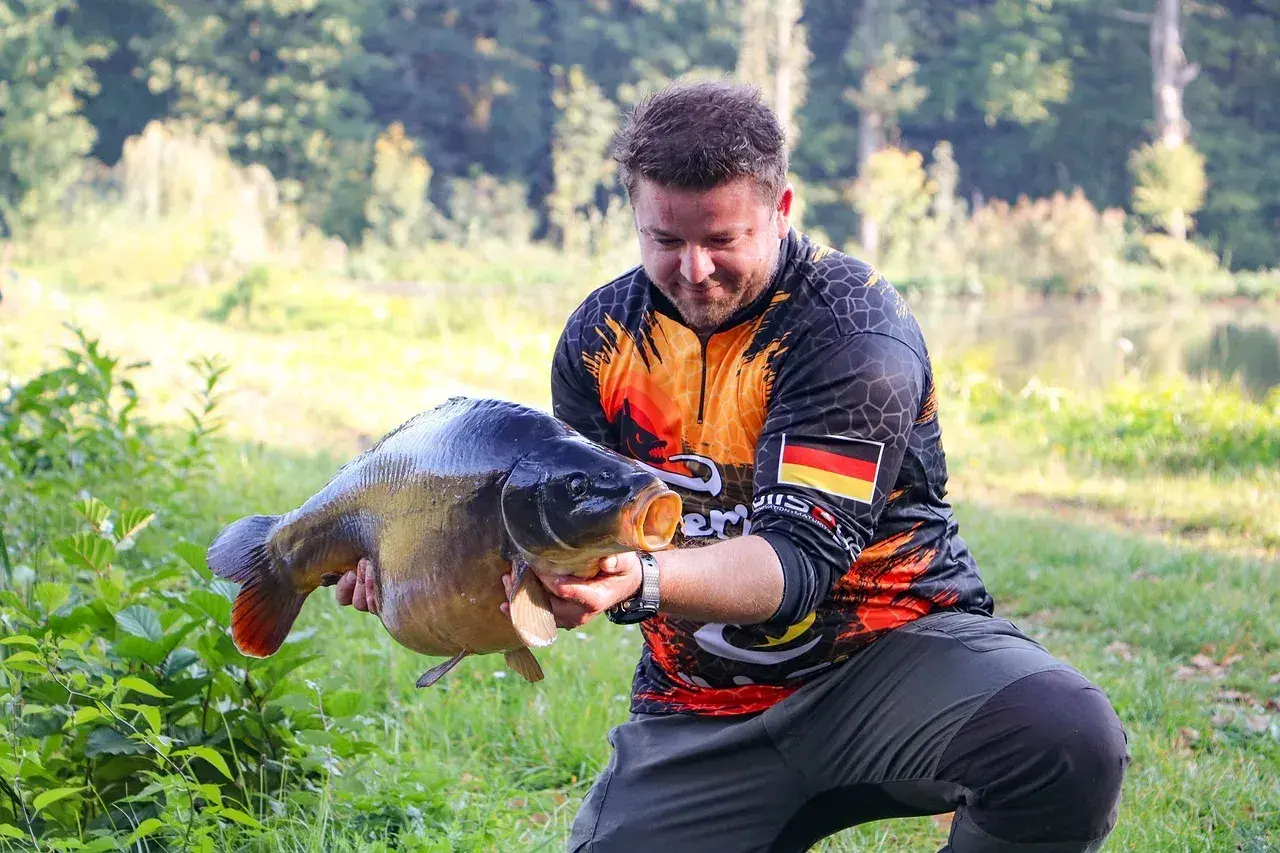 Wędkarz z dumą prezentuje okazałego karpia, który z pewnością nie jest ani sieją, ani sielawą.