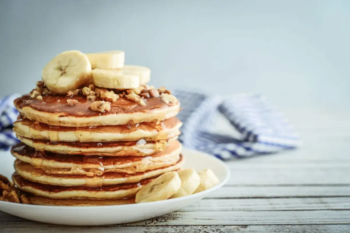 Una pila de tortitas de plátano cubiertas de miel y nueces, con rodajas de plátano fresco encima.