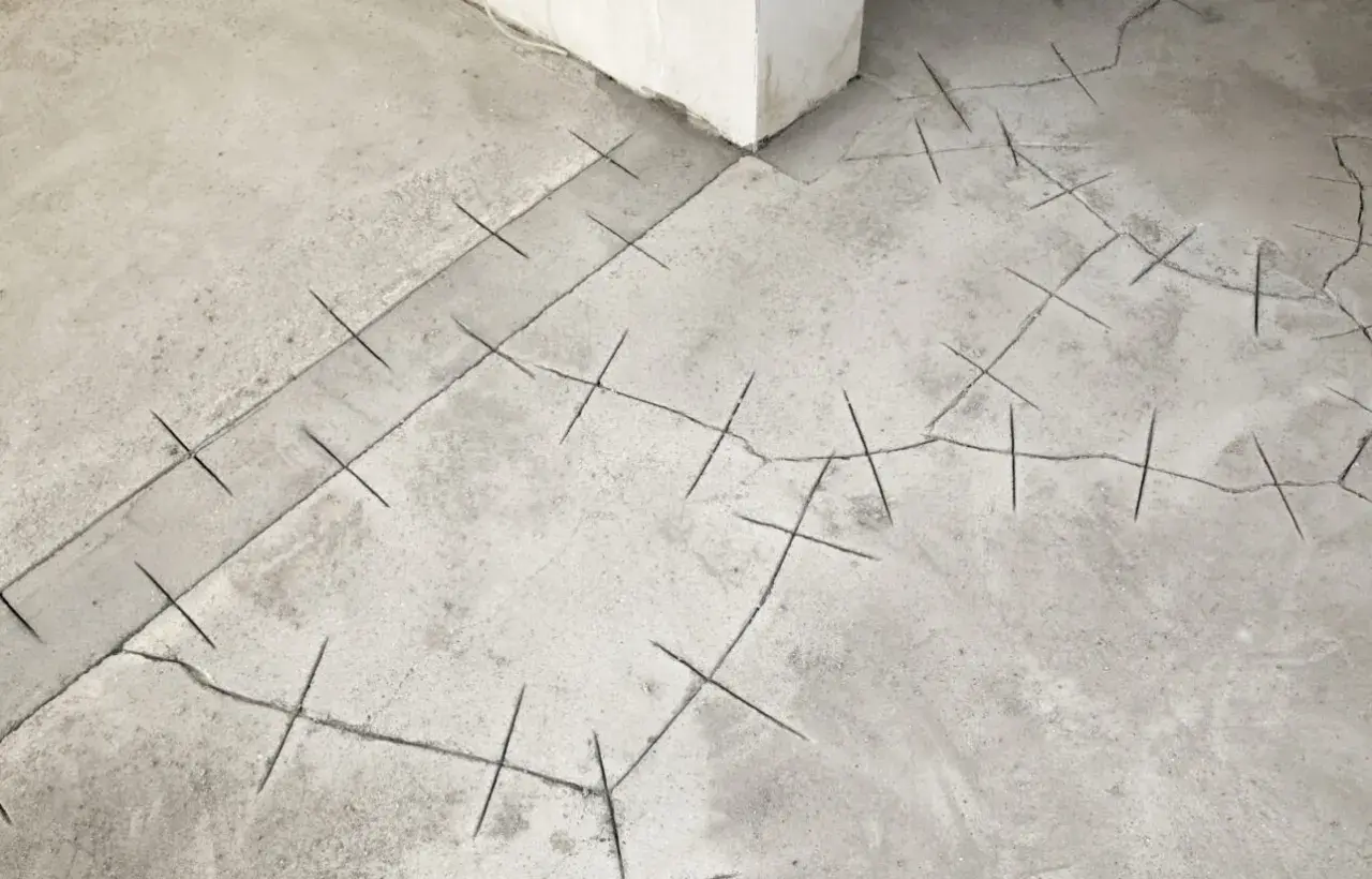 Risse in der Bodenplatte eines Altbaus, markiert mit Kreuzschraffuren zur Rissbreitenmessung.