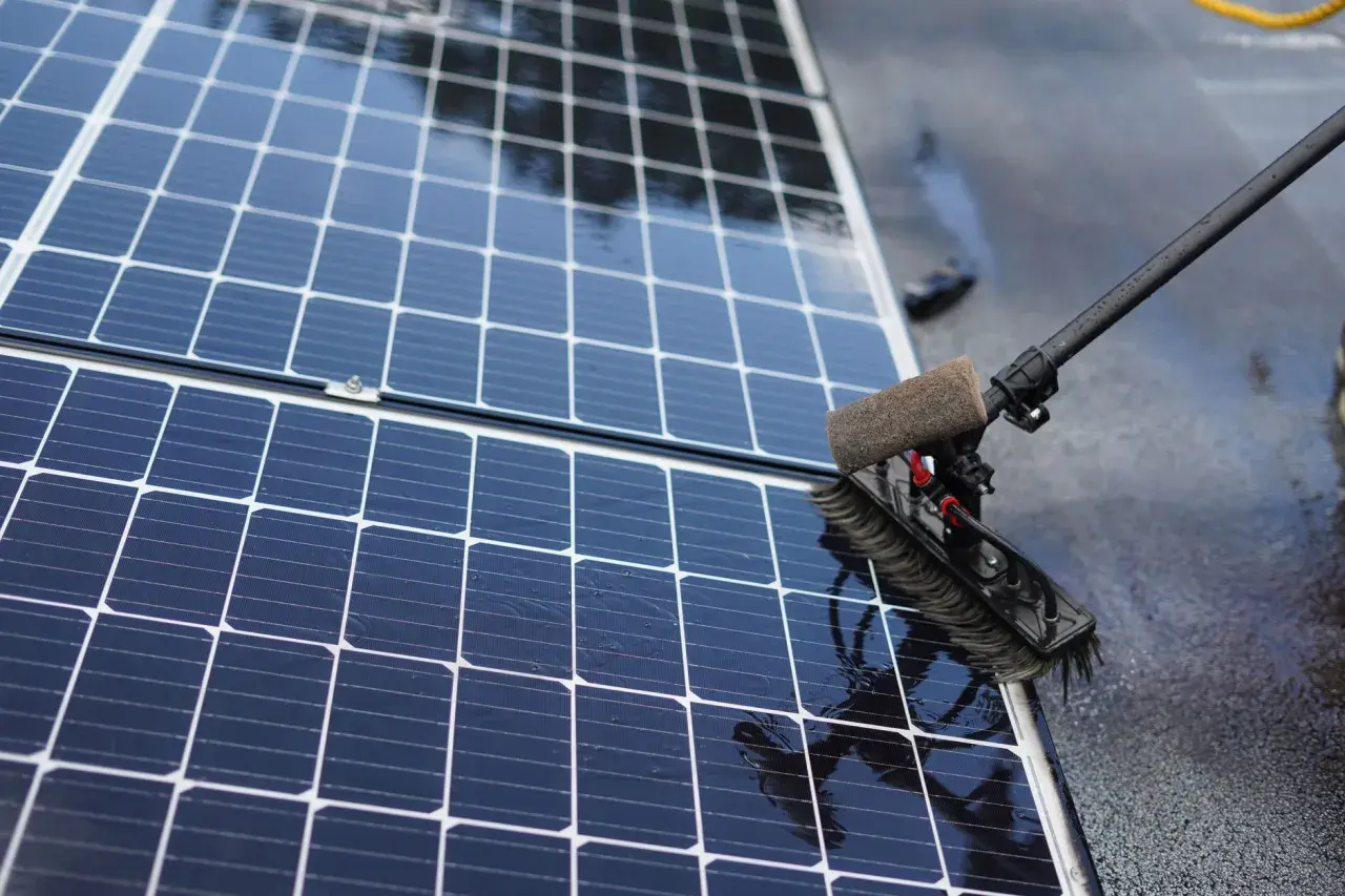 Brosse rotative en action pour nettoyer panneau solaire. L'eau ruisselle sur les cellules bleues et brillantes.