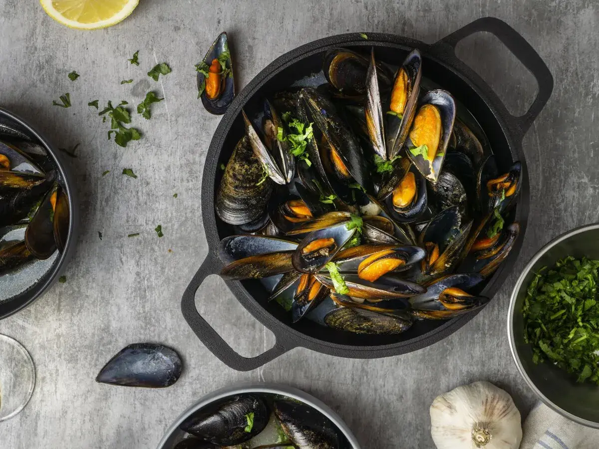 Una deliciosa preparación de mejillones, mostrando que son los mejillones, servidos en una sartén negra con perejil fresco y limón.