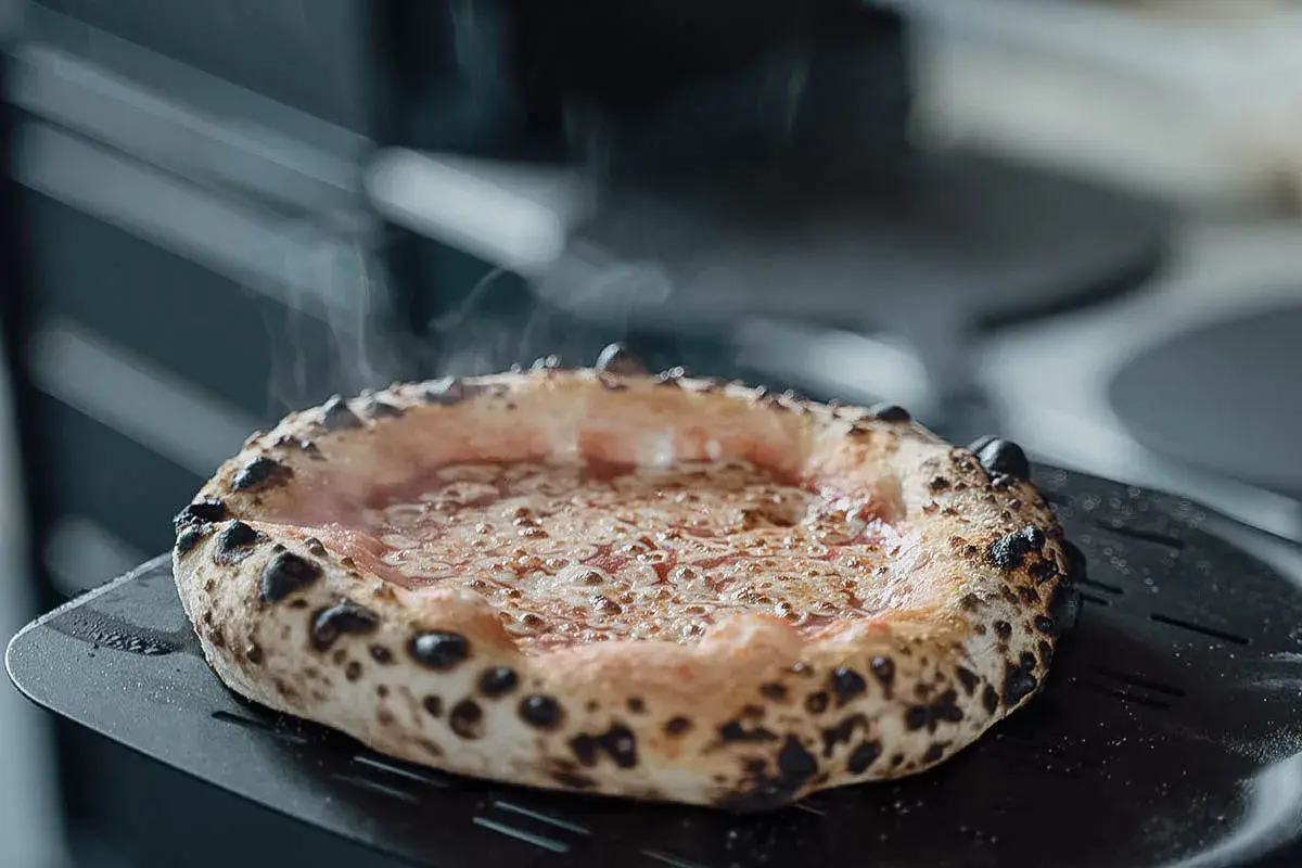 Frisch gebackene Pizza mit dampfendem Käse auf einem Pizzaschieber. Eine von vielen köstlichen Pizza sorten, bereit zum Servieren.