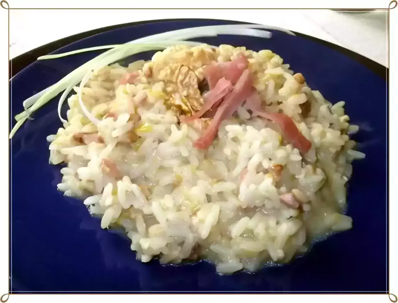 Un cremoso risotto pere e speck, guarnito con noci e fili di porro.