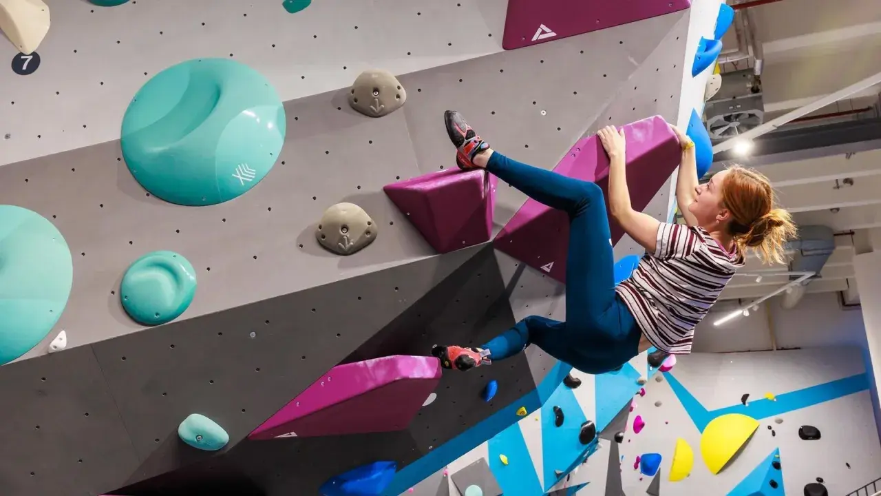 Frau klettert an einer bunten Wand in einer Boulderhalle in Hamburg. Sie hält sich an einem pinken Griff fest.