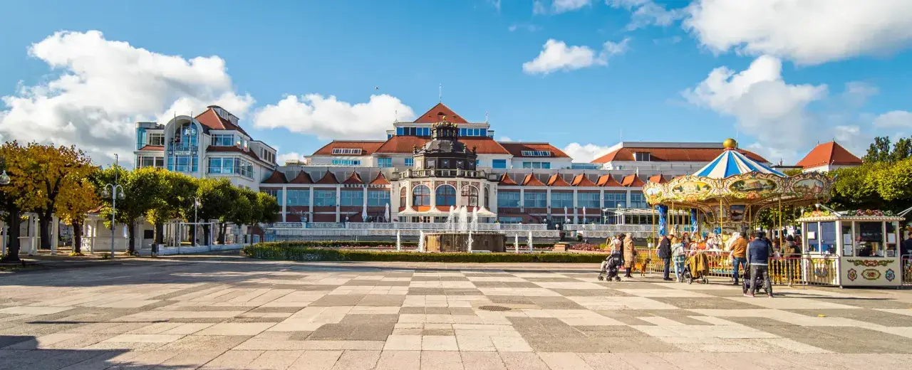 Sopot, część Trójmiasta, co to za miejsce? Plac z karuzelą i fontanną przed pięknym budynkiem.