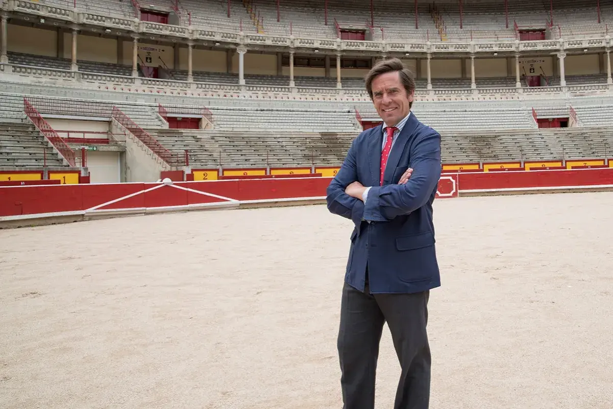 Eduardo Dávila Miura, con traje azul y corbata roja, posa en el ruedo de una plaza de toros.