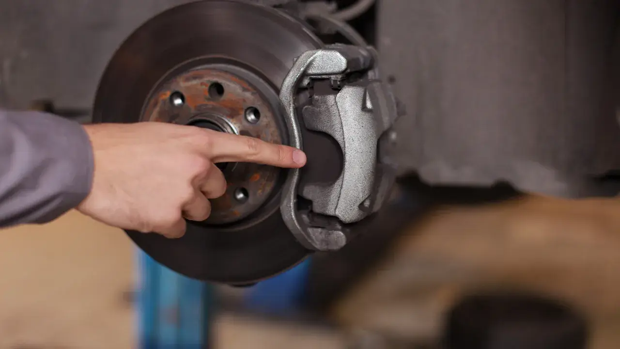 A mechanic's finger points to the dot brake pad thickness, indicating it's time for a replacement.