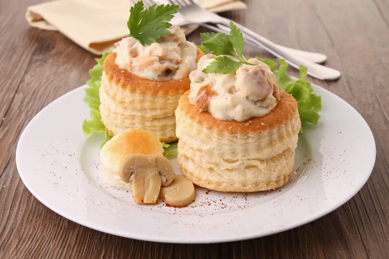 Deux vol-au-vent poulet crémeux, garnis d'une sauce onctueuse et de morceaux de poulet, décorés de persil frais et accompagnés de champignons.