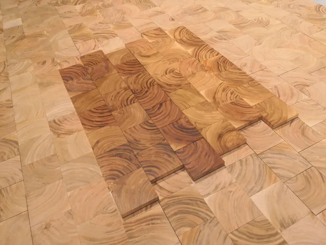 Patrón de suelo de madera cerezo con vetas circulares, algunas piezas más oscuras que otras, creando un efecto de degradado.
