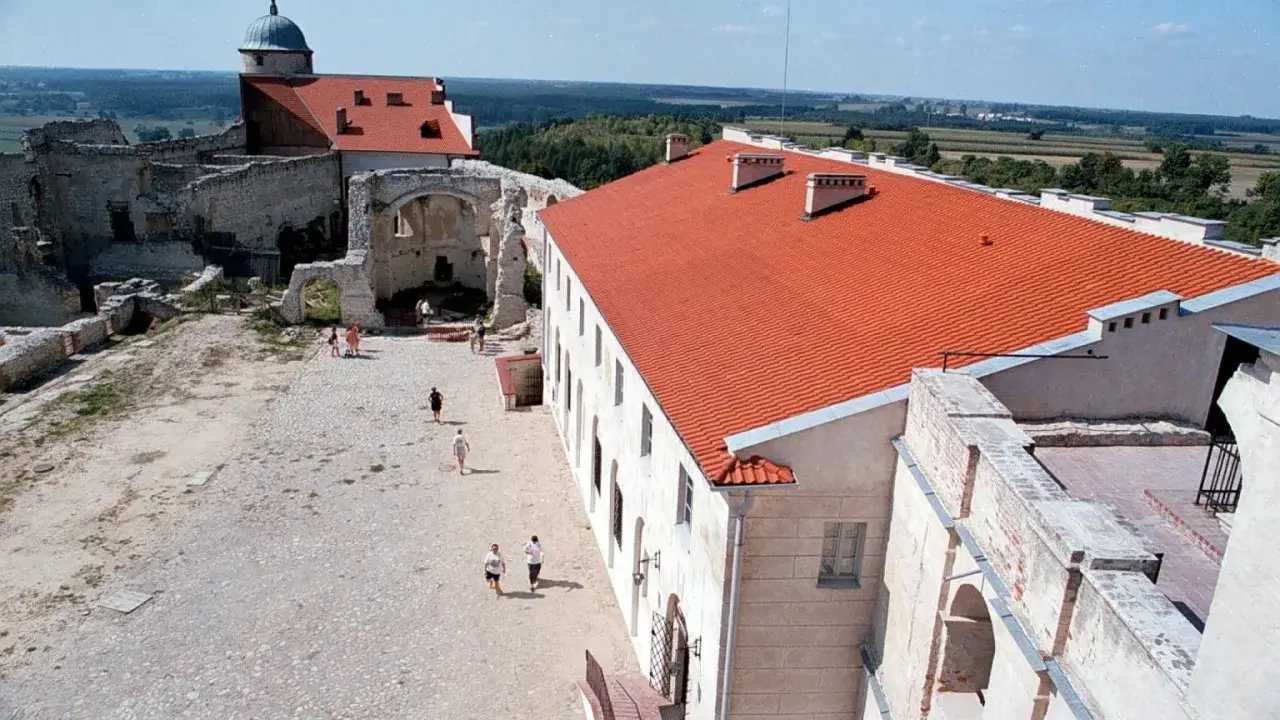 Dziedziniec zamku w Janowcu z ruinami i odrestaurowanym budynkiem z czerwonym dachem.