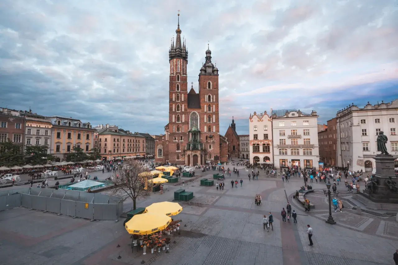Rynek Główny w Krakowie, z Bazyliką Mariacką w centrum, to jeden z krakowskich top attractions. Ludzie spacerują, a żółte parasole tworzą barwne plamy.