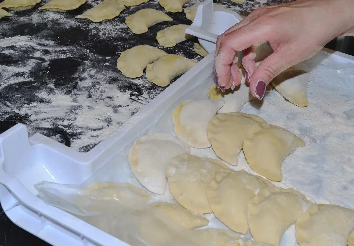 Ręka układa pierogi na tacy, posypanej mąką. Aby ugotowane pierogi się nie skleiły, warto je od razu po ugotowaniu delikatnie polać tłuszczem.