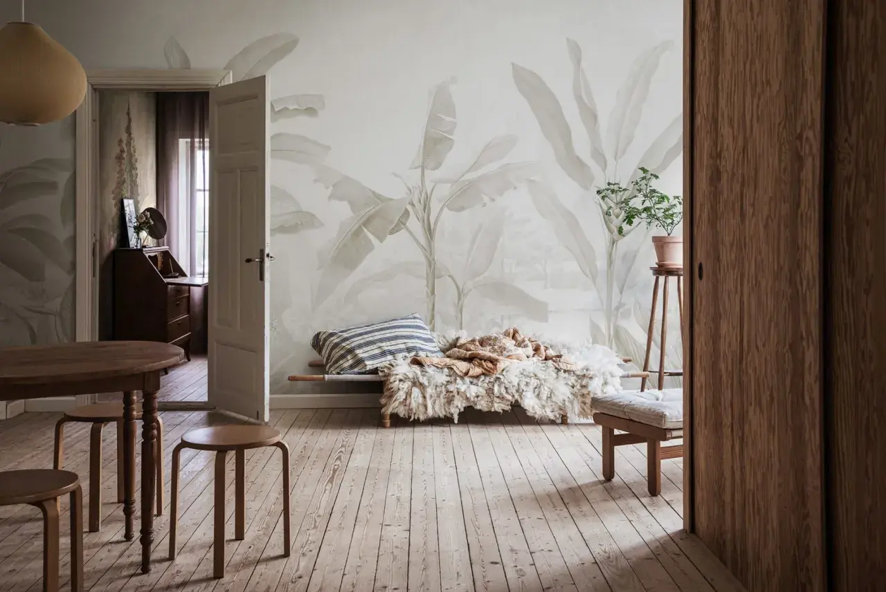 Salon w stylu boho z tapetą w liście bananowca, drewnianymi meblami i przytulnym legowiskiem.