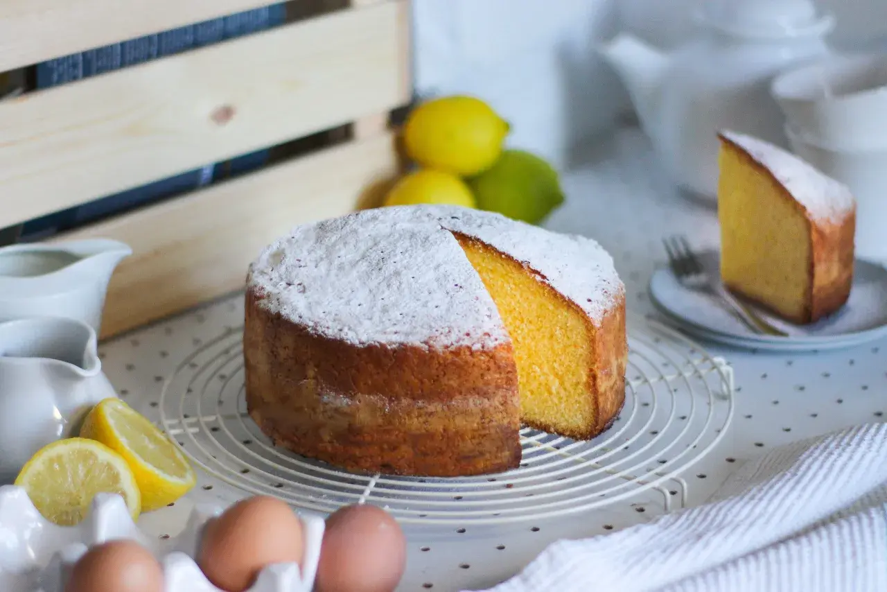 Una torta paradiso sofficissima, cosparsa di zucchero a velo, con spicchi di limone e uova fresche.