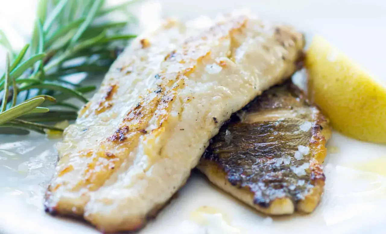 Zander grillen: Zwei saftige Filets mit knuspriger Haut, garniert mit Rosmarin und einer Zitronenspalte. Perfekt gegrillt!