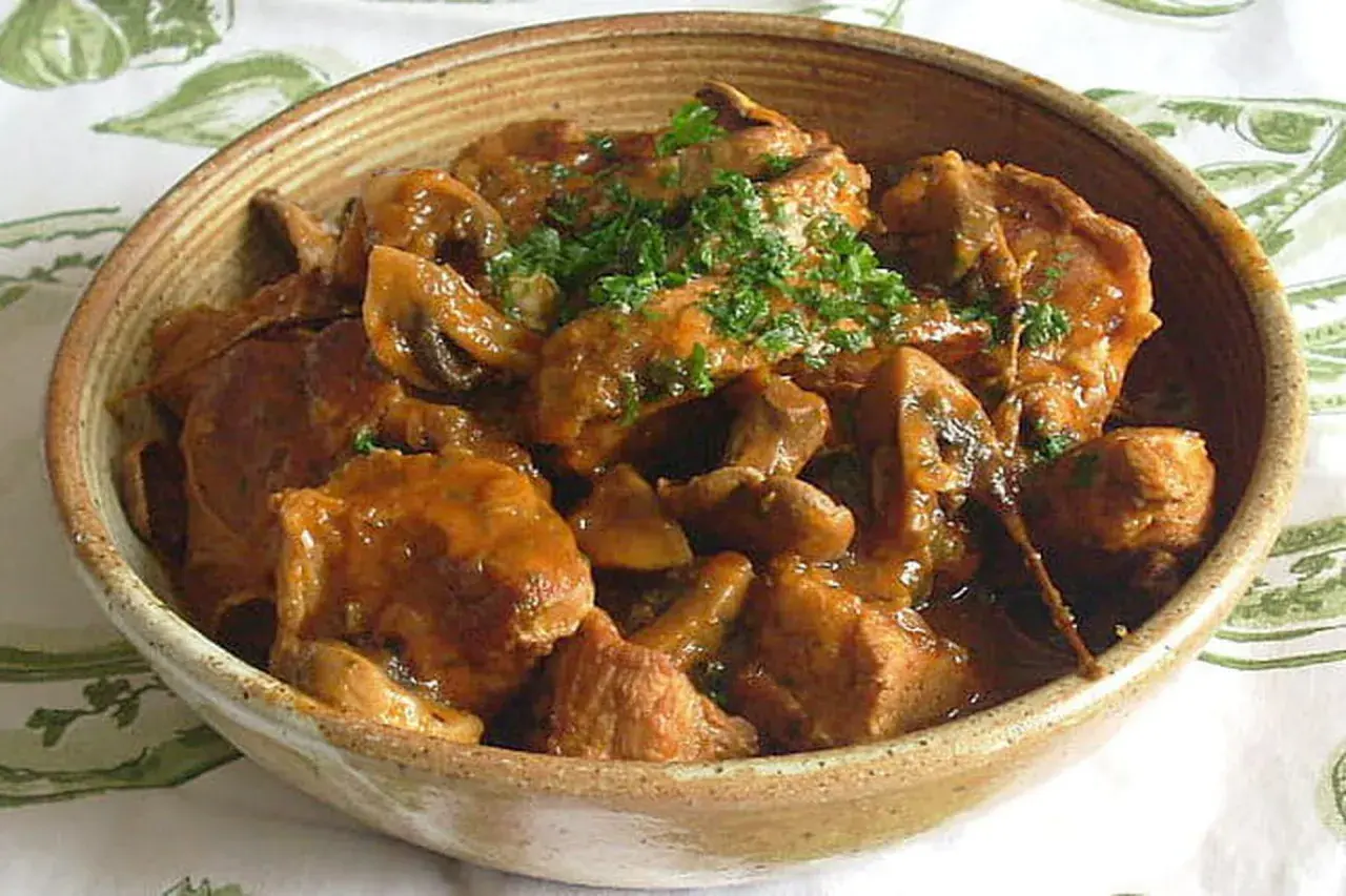 Un délicieux sauté de veau aux champignons, garni de persil frais, servi dans un bol en terre cuite.