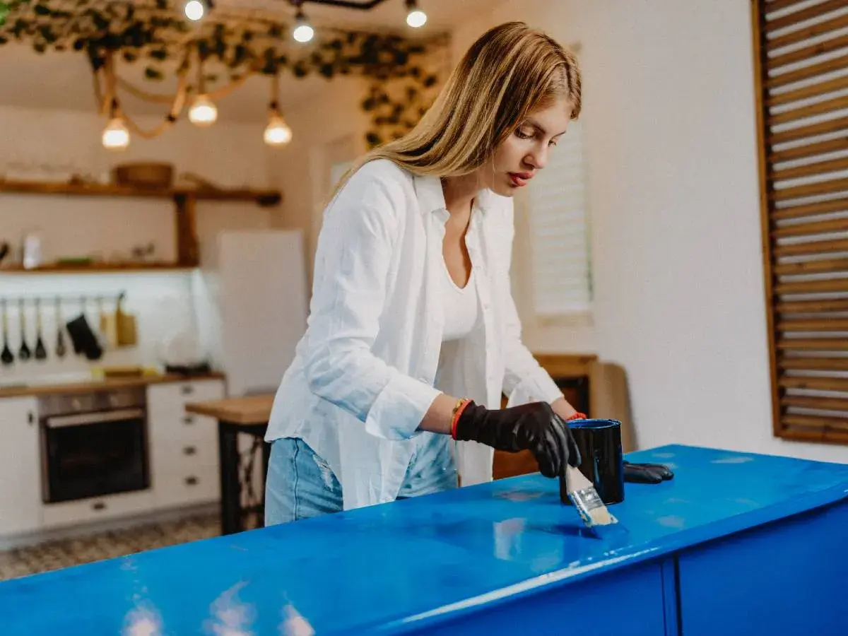 Donna con guanti neri applica vernice blu su un mobile, trasformandolo per rendere opaco un mobile lucido.