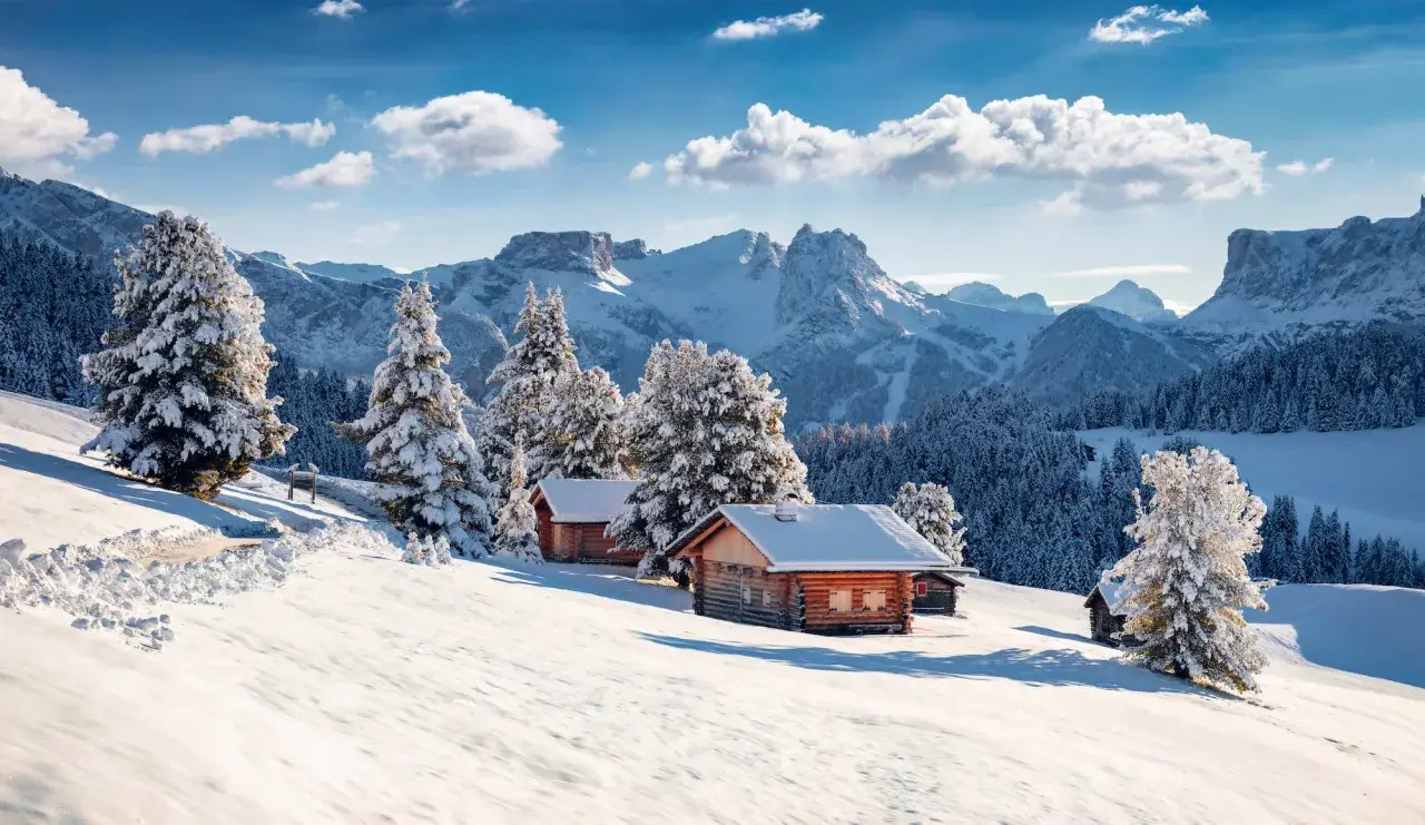 Chalets enneigés sous un ciel bleu, au cœur d'une **caravaneige massif central**. Sapins couverts de neige, montagnes majestueuses en arrière-plan.
