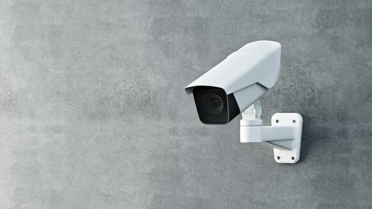 Une caméra de surveillance blanche est fixée sur un mur de béton. Cette caméra sans internet assure une sécurité discrète.