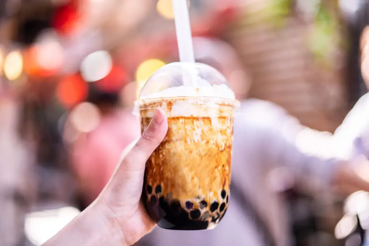 Ręka trzyma kubek z brązowym bubble tea. Czy bubble tea jest zdrowe? Zależy od składników, ale ten wygląda pysznie!