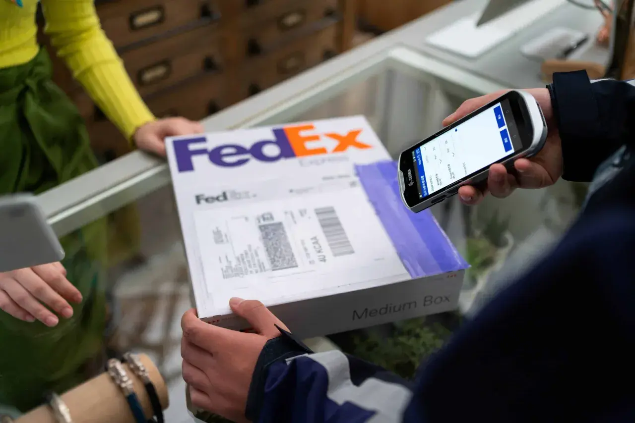 Osoba skanuje kod kreskowy na paczce FedEx za pomocą urządzenia mobilnego, realizując pointpack śledzenie.