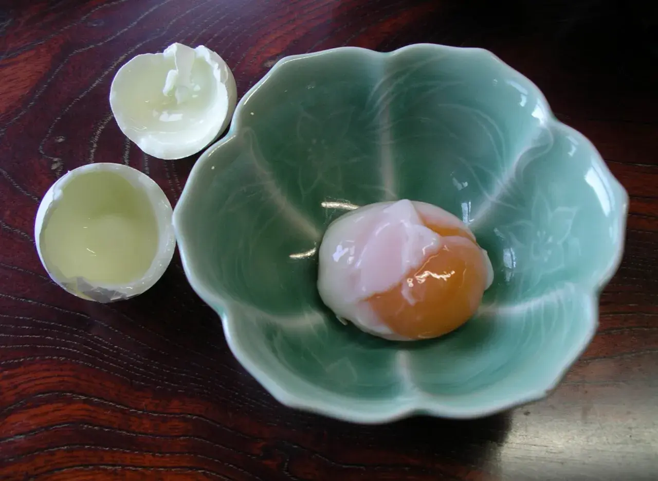 A perfectly soft-boiled egg, a delicacy of Japanese eggs, rests in a green, petal-shaped bowl.