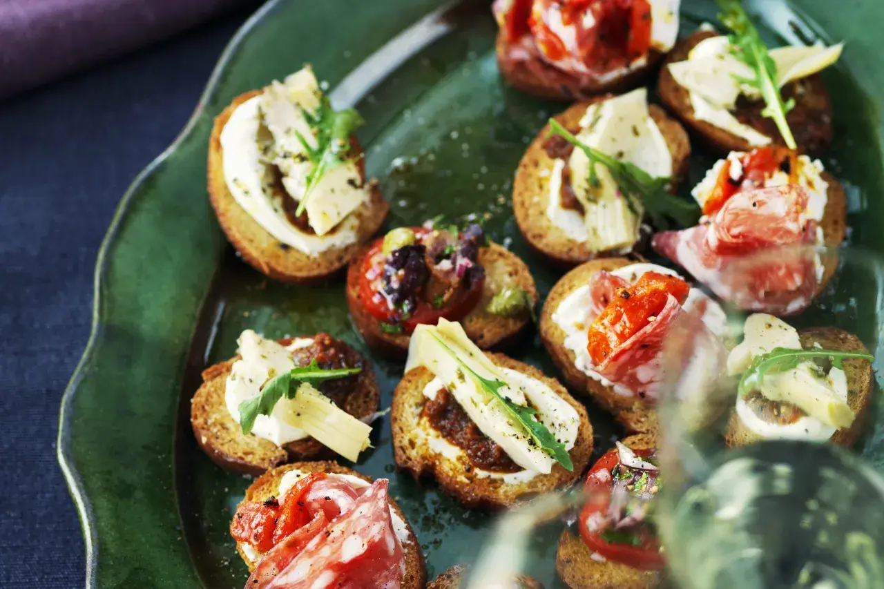 En grön tallrik med olika crostini topping: salami, tomat, ost och ruccola.
