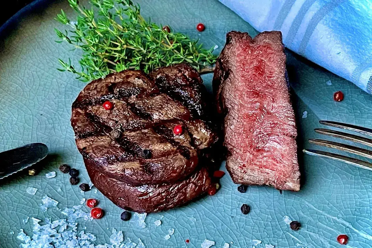 Perfekt gegrilltes Rinderfilet mit zarten rosa Kern, garniert mit frischem Thymian und bunten Pfefferkörnern. Ein Genuss für jeden Fleischliebhaber.